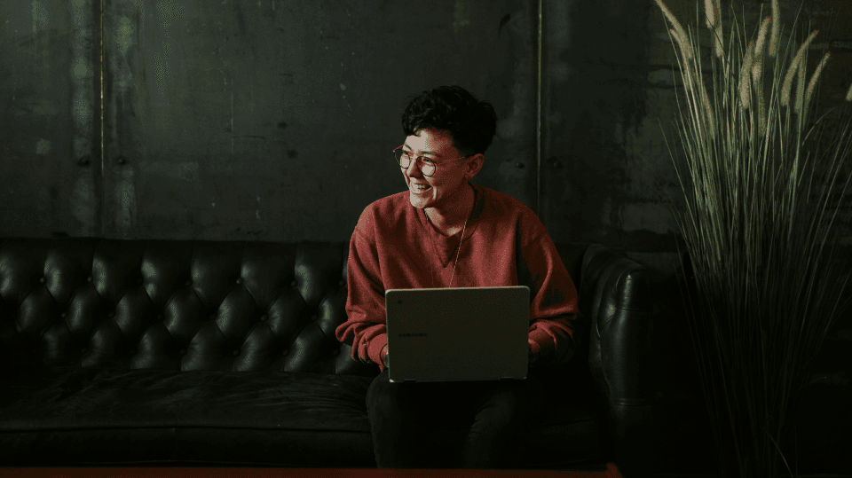 Uśmiechnięta osoba pracująca na laptopie w nowoczesnym wnętrzu, symbolizująca rozwój biznesu online i elastyczność pracy zdalnej.